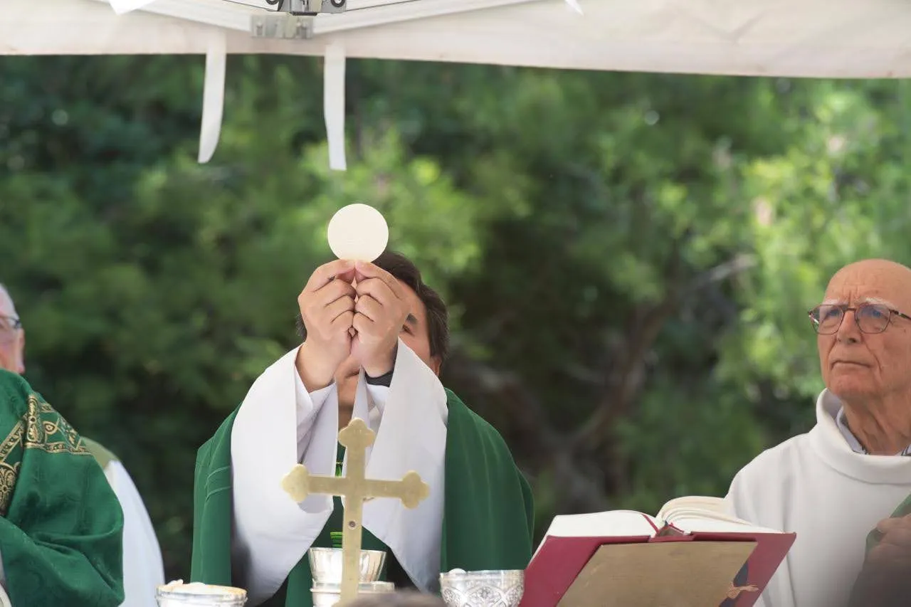 Le prêtre élève l'hostie lors de la consécration, pendant une messe en plein air